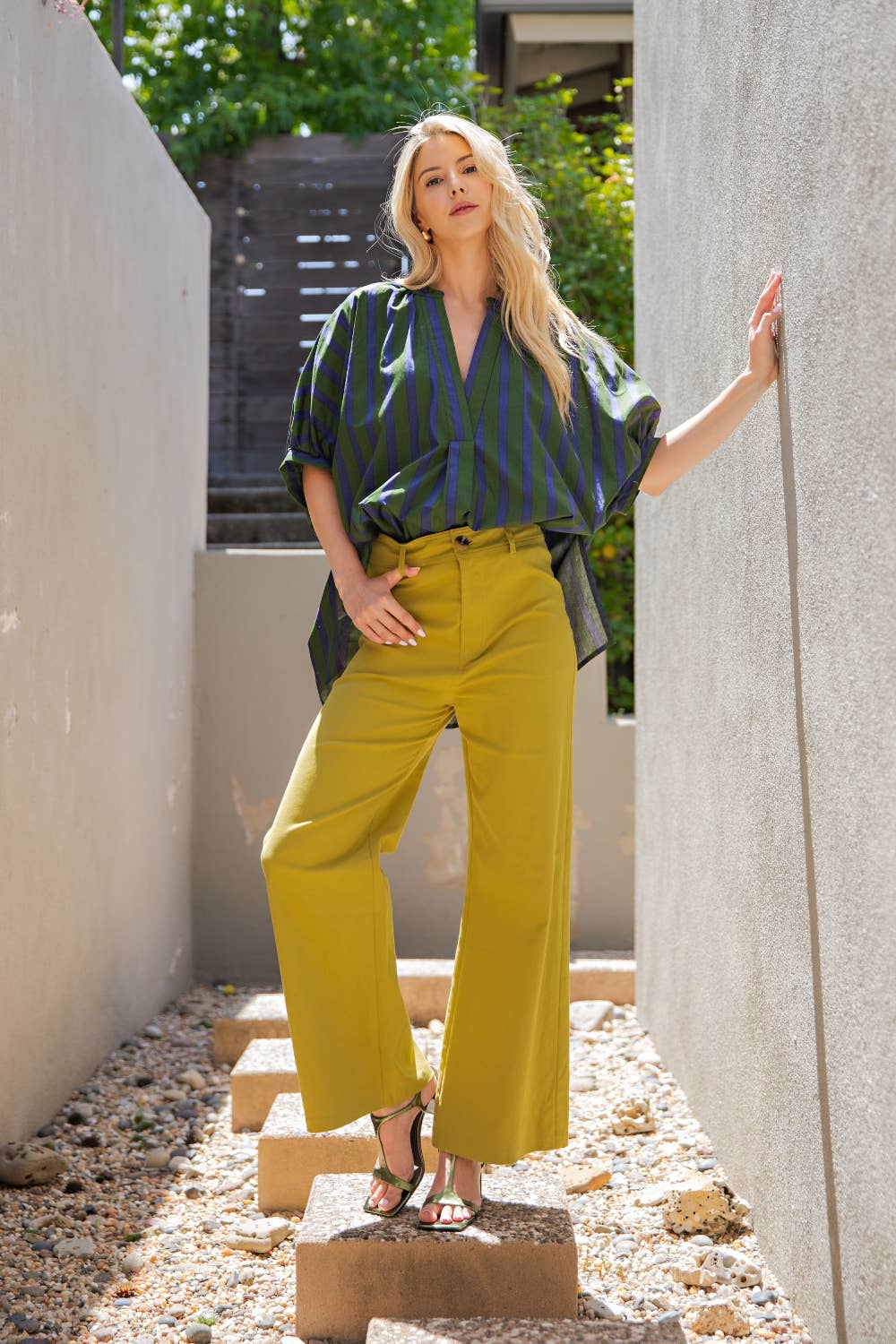 Woman in a green striped shirt and yellow pants standing in an outdoor setting.