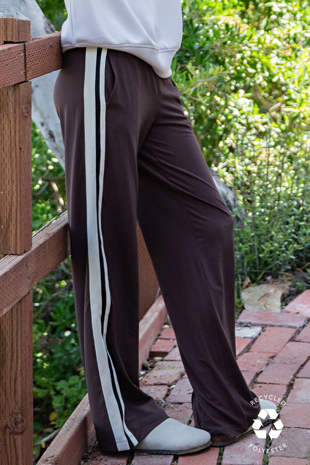 Brown pants with white stripes worn by a person on a wooden deck with greenery in the background