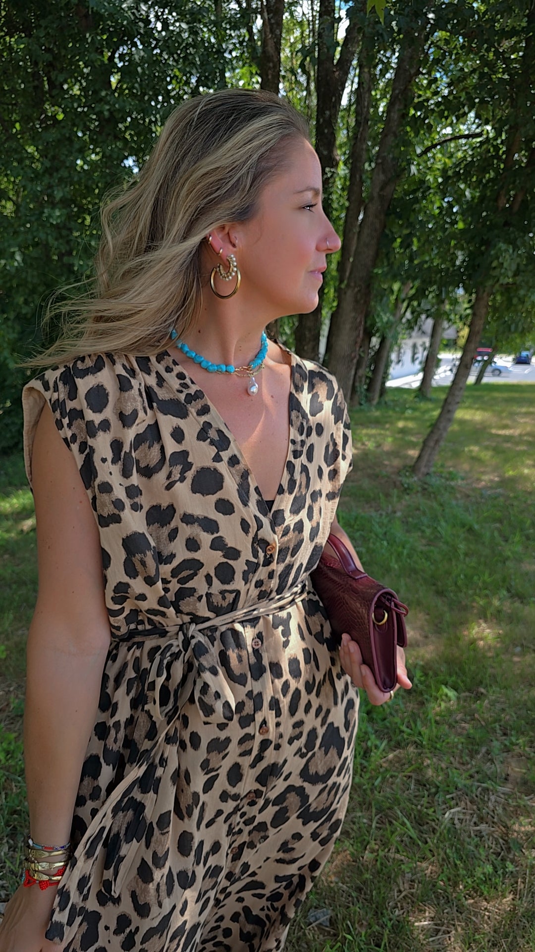 Woman in a leopard print dress standing outdoors with trees and grass in the background