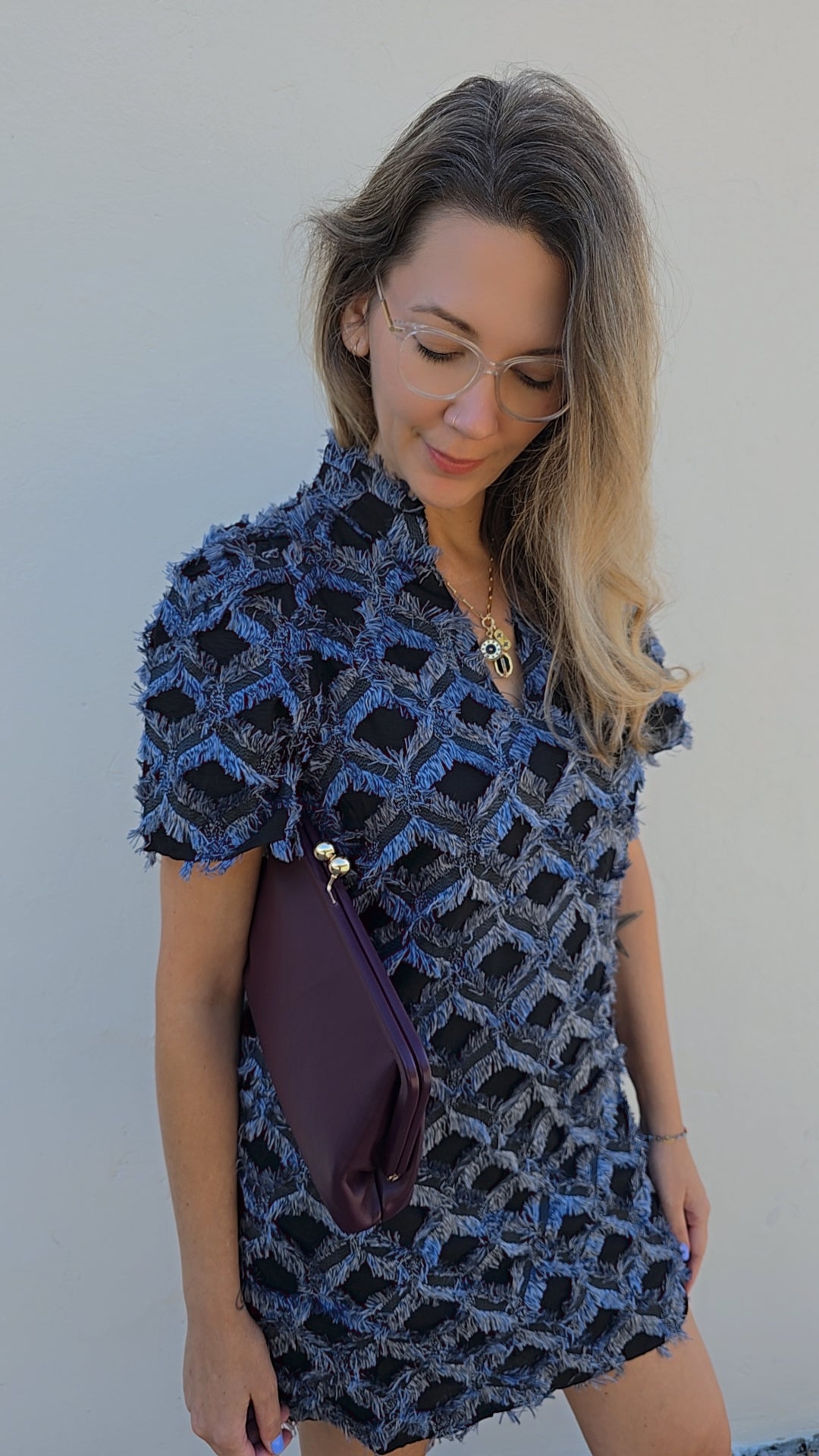 Woman wearing a blue patterned dress holding a purple bag against a light background