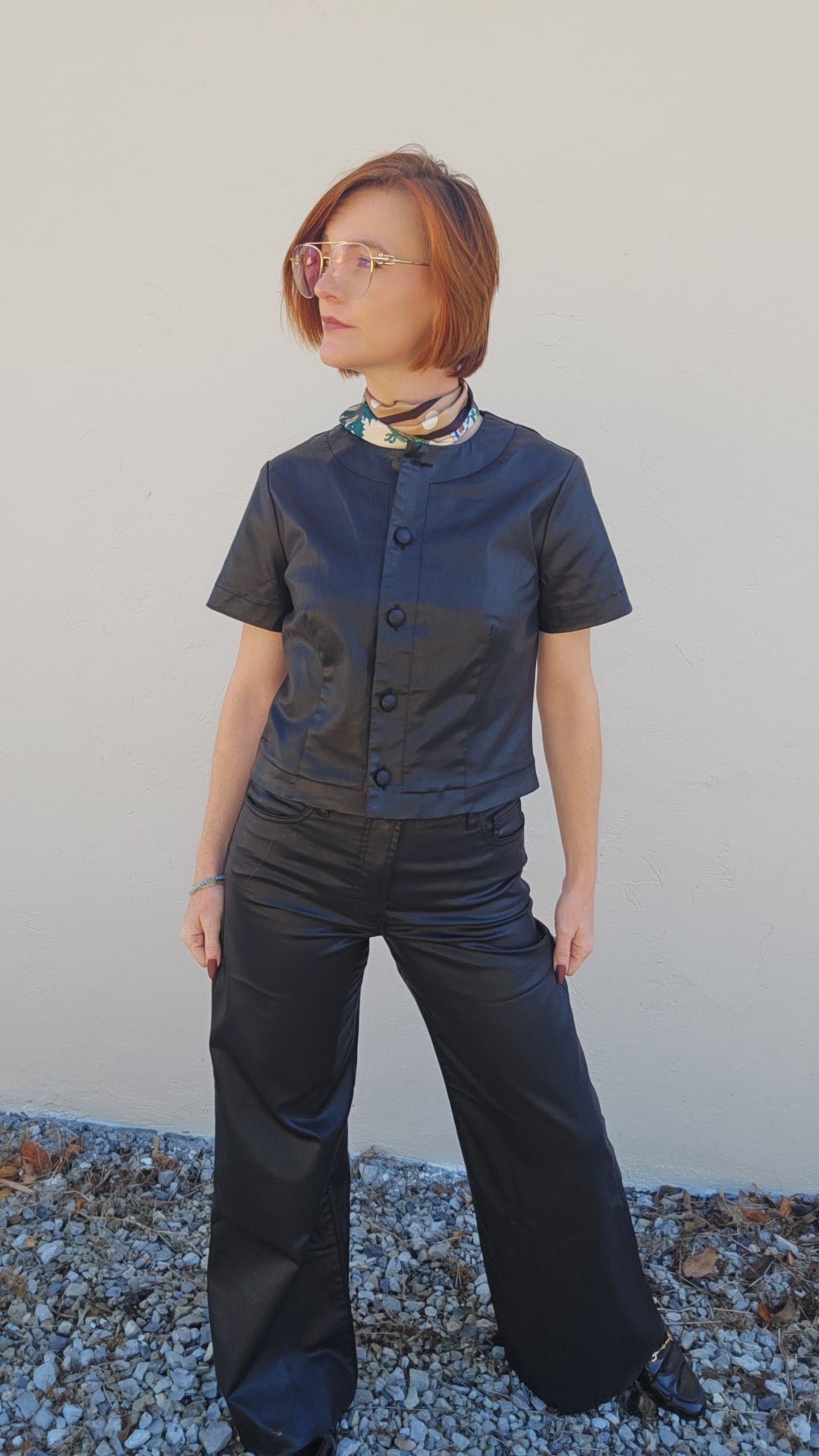 Person wearing a black outfit with a patterned scarf against a plain background