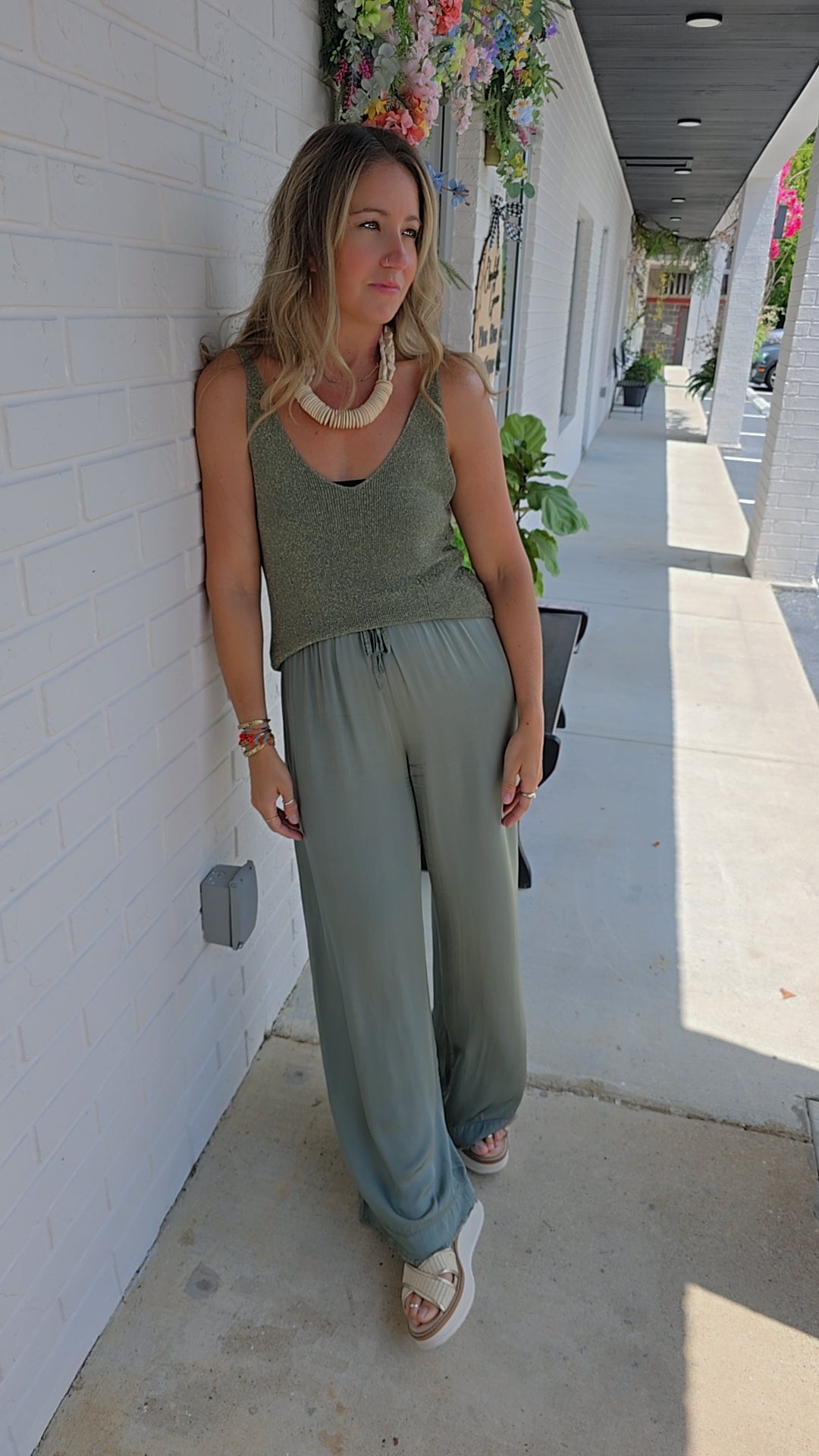 Woman in a green outfit standing against a white wall.