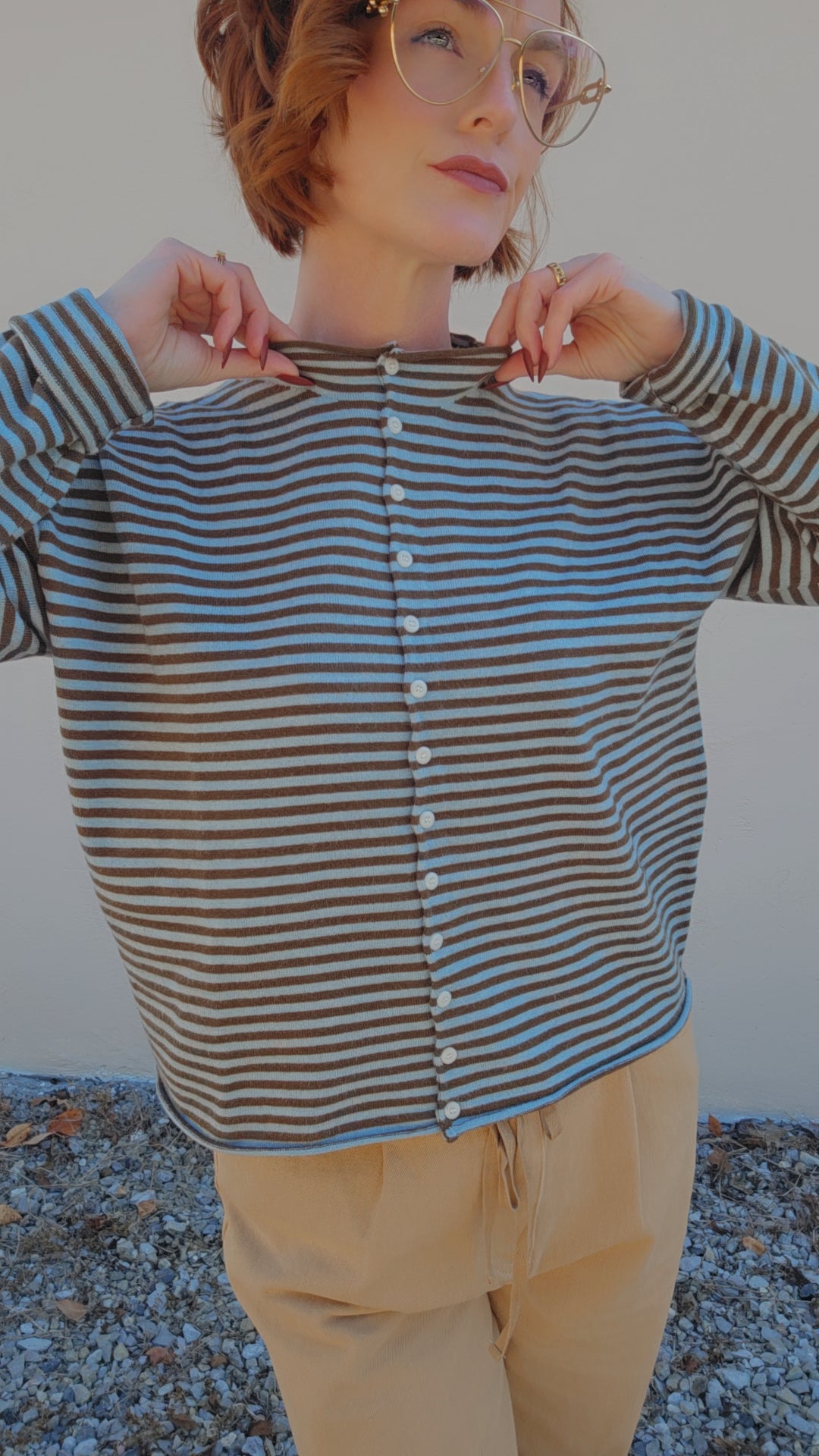 Person wearing a striped shirt and beige pants against a neutral background