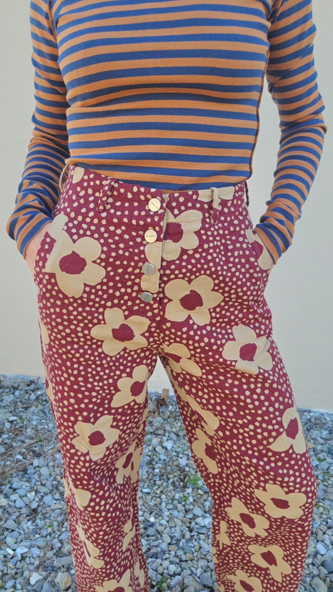 Person wearing a striped shirt and floral pants standing on a gravel surface.