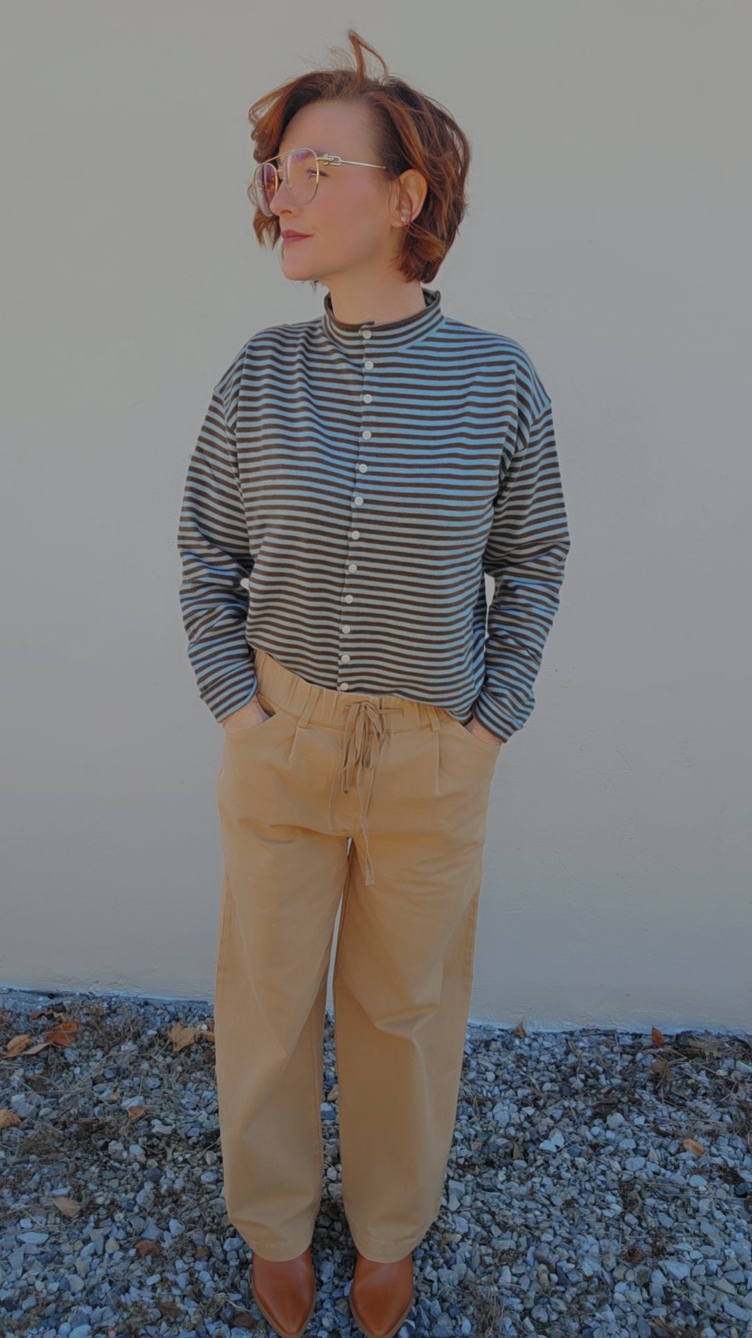 Person wearing a striped shirt and beige pants standing against a plain background