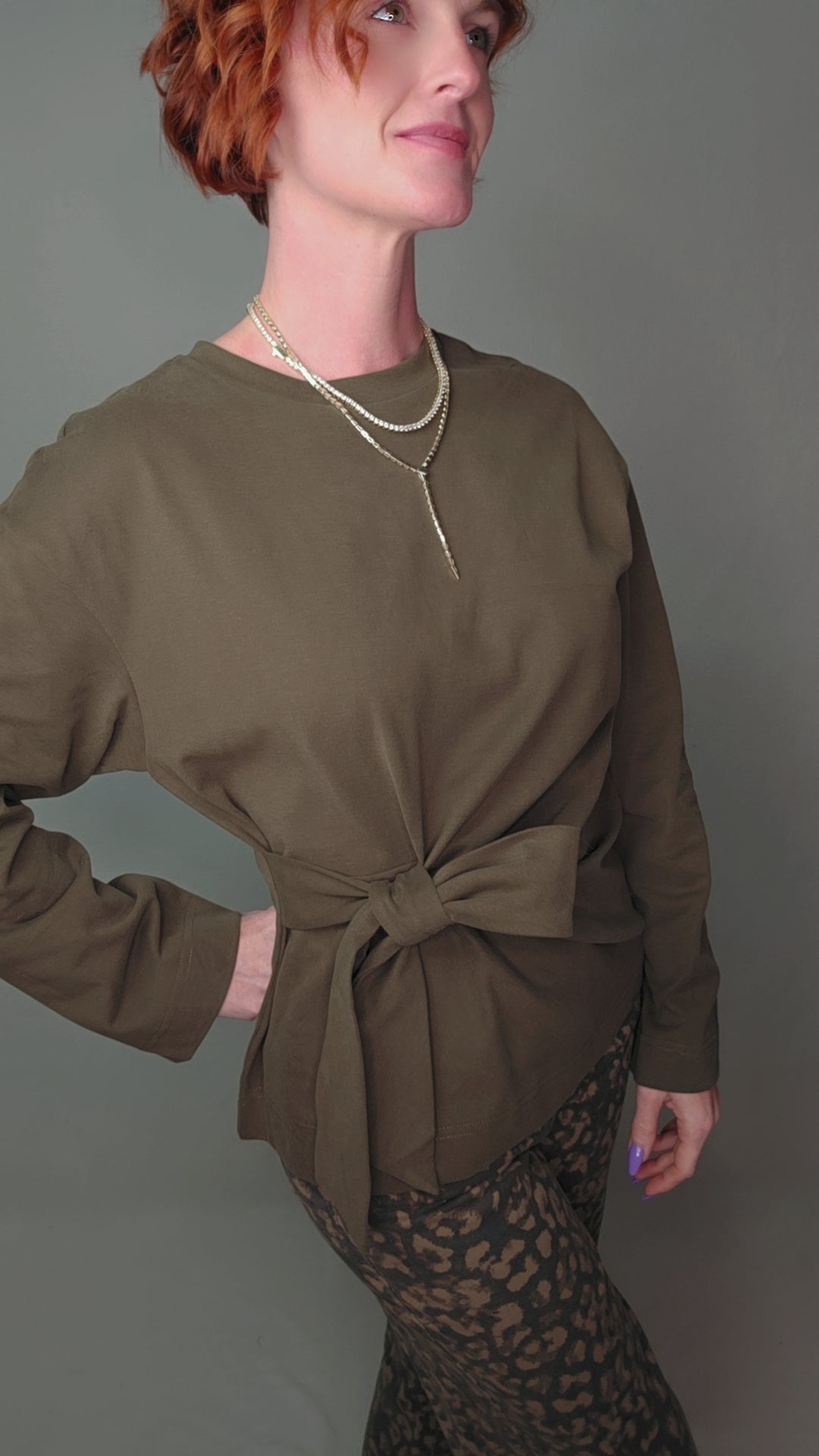 Person wearing an olive green long-sleeve top with a tie detail on a gray background