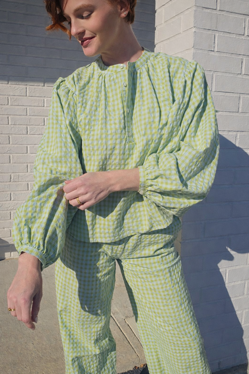 Person wearing a green checkered outfit standing against a brick wall.