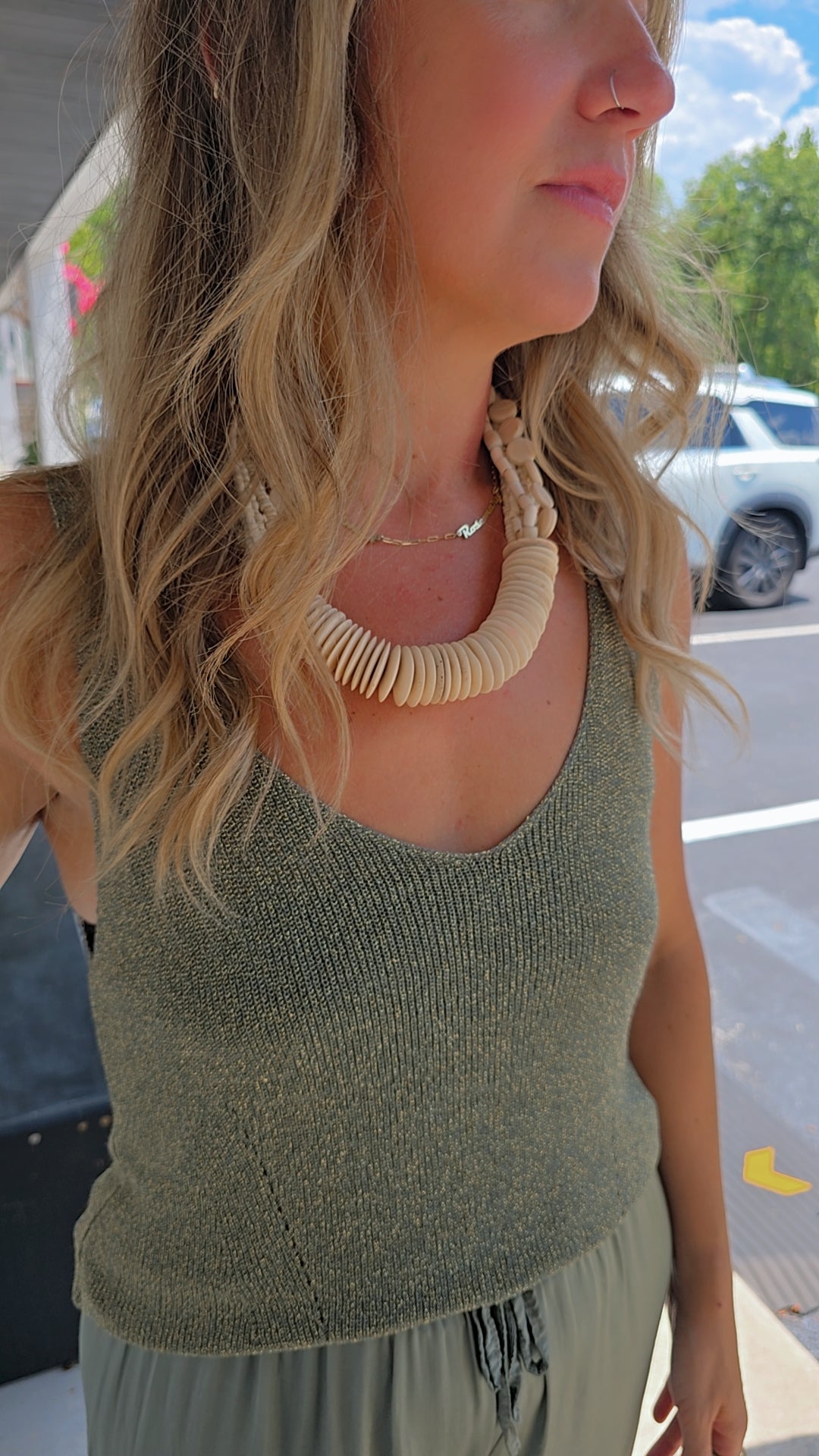 Woman wearing a green sleeveless top and beige necklace outdoors