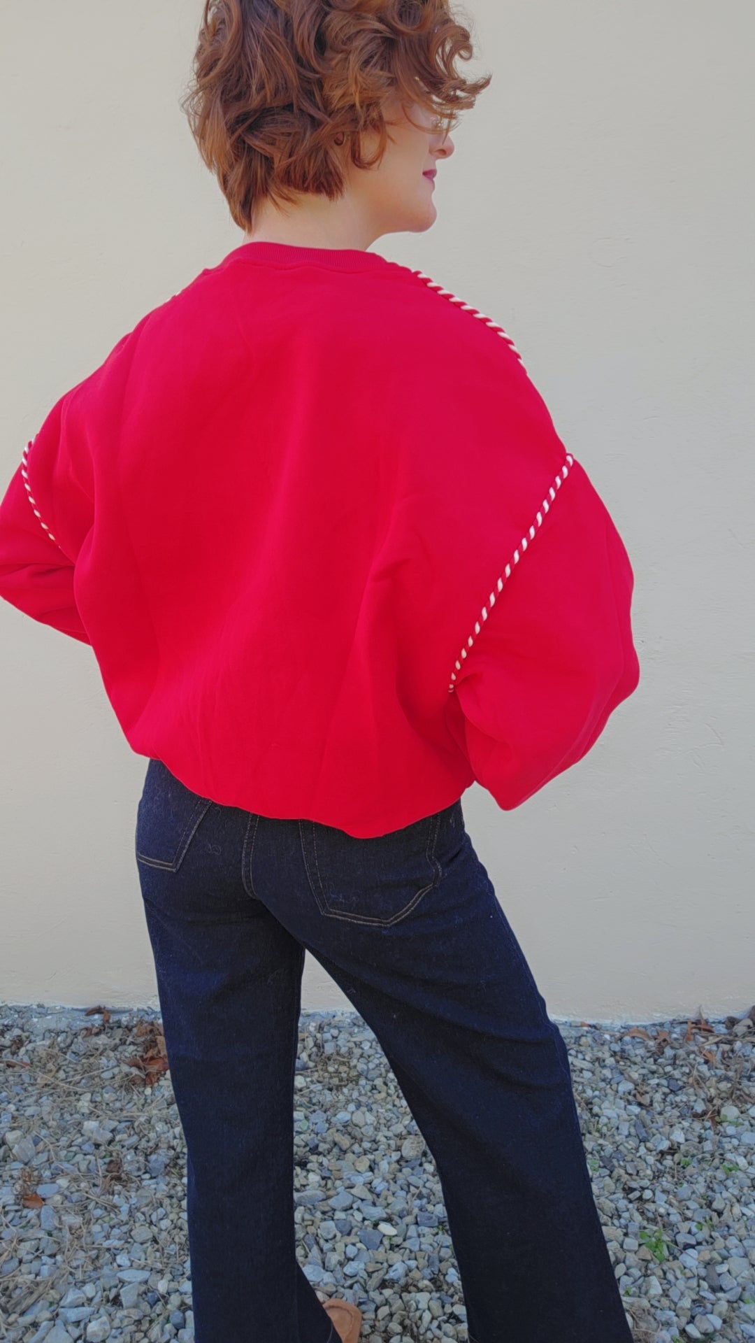 Person wearing a bright pink sweater with white trim and dark blue jeans against a plain background