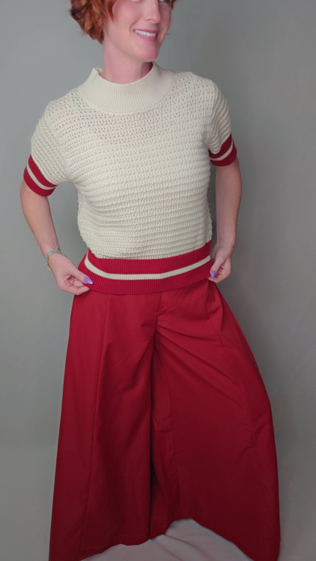 Person wearing a cream sweater with red stripes and red pants against a gray background