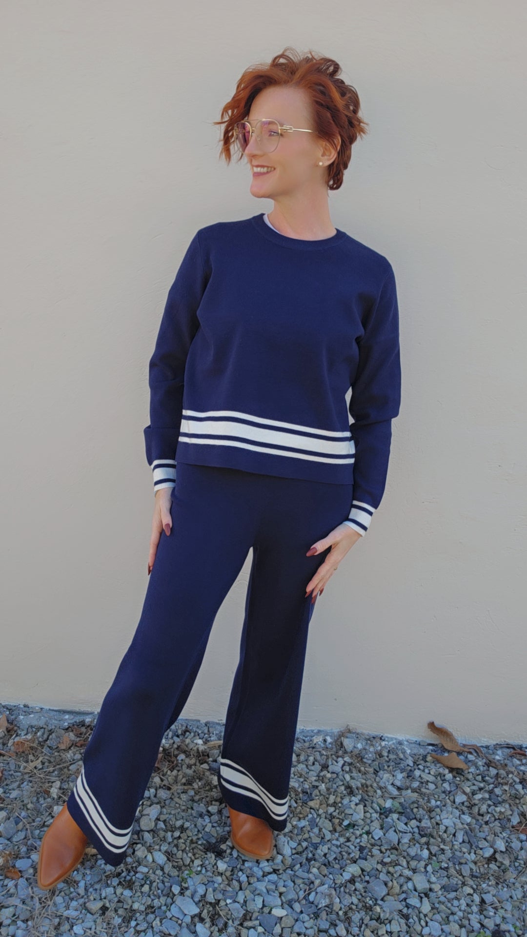 Woman wearing a blue sweater and pants with white stripes standing on a textured surface.