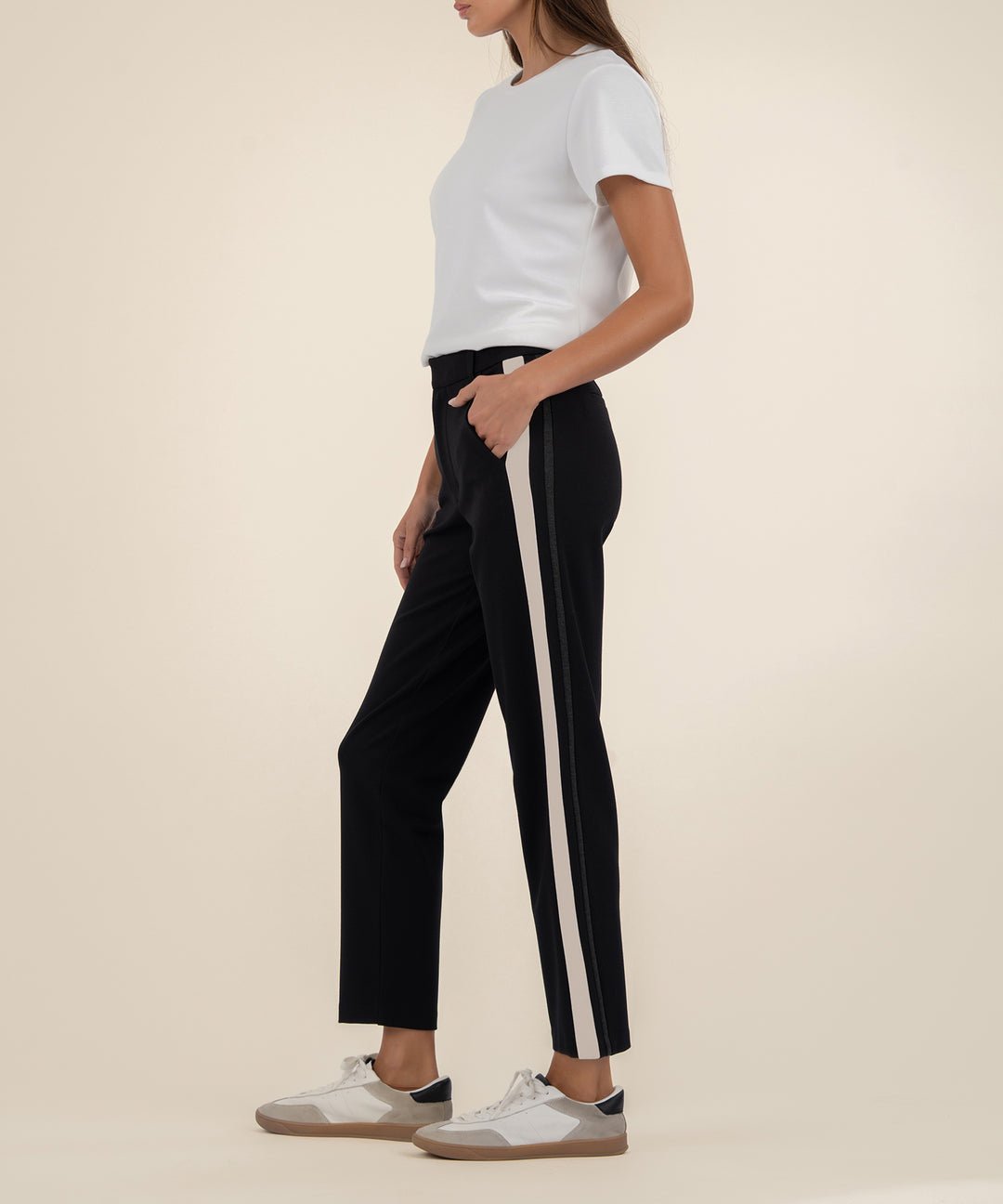 Person wearing black pants with a white stripe and a white shirt on a beige background
