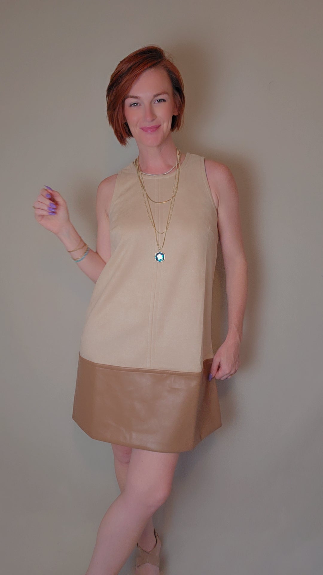 Woman wearing a beige sleeveless top and brown leather skirt against a plain background